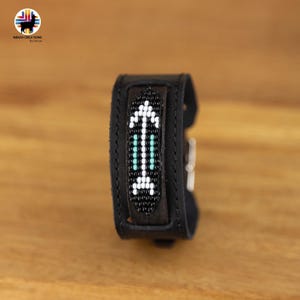 Può includere: Braccialetto in pelle nera con un design a freccia con perline bianche e turchesi.