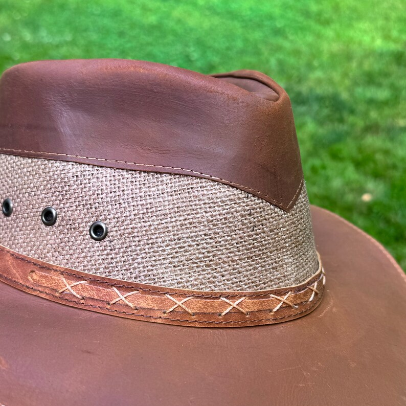 May include: A brown leather cowboy hat with a woven fabric band and a stitched leather trim.