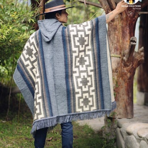 May include: A gray hooded poncho with a geometric pattern in white, brown, and blue. The poncho has a fringe border and is worn by a person wearing a brown hat and blue jeans.