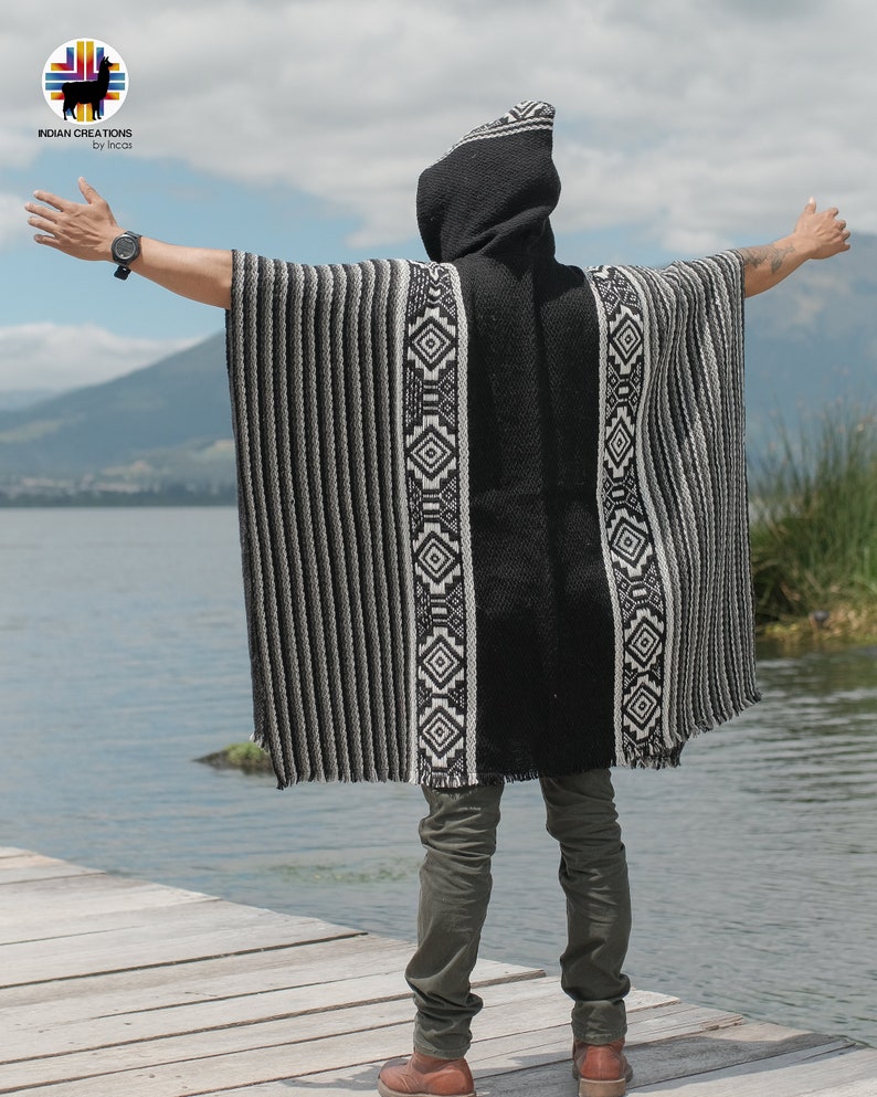 Pode incluir: Uma pessoa vestindo um poncho com capuz listrado preto e branco com padr&otilde;es geom&eacute;tricos. O poncho &eacute; feito de um material macio e quente e tem um caimento relaxado. A pessoa est&aacute; em p&eacute; em um p&iacute;er de madeira com vista para um corpo de &aacute;gua.