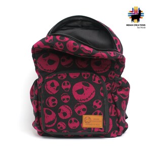K&ouml;nnte beinhalten: Ein schwarzer und pinkfarbener Rucksack mit einem sich wiederholenden Muster von Jack Skellingtons Gesicht aus dem Film Nightmare Before Christmas. Der Rucksack hat eine Rei&szlig;verschlusstasche auf der Vorderseite und einen schwarzen Rei&szlig;verschluss.