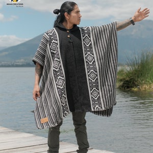 Pode incluir: Um poncho listrado preto e branco com padr&otilde;es geom&eacute;tricos. O poncho &eacute; feito de l&atilde; de alpaca e tem capuz. O modelo est&aacute; usando o poncho sobre uma camisa preta e cal&ccedil;as jeans verde-escuras.