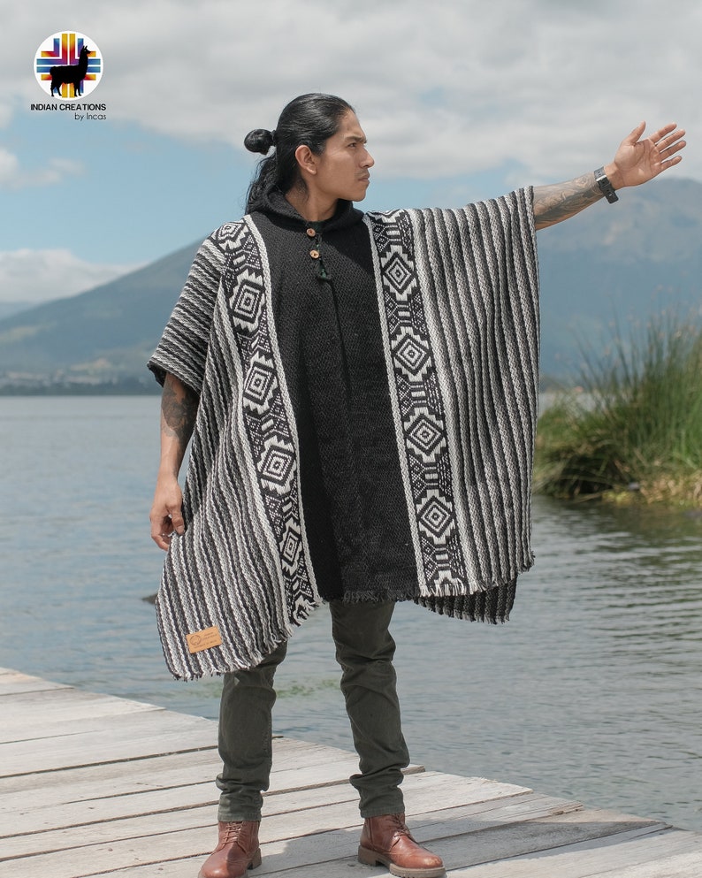 Pode incluir: Um poncho listrado preto e branco com padr&otilde;es geom&eacute;tricos. O poncho &eacute; feito de l&atilde; de alpaca e tem capuz. O modelo est&aacute; usando o poncho sobre uma camisa preta e cal&ccedil;as jeans verde-escuras.