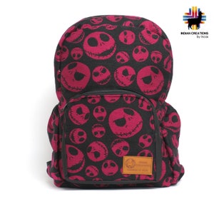 K&ouml;nnte beinhalten: Ein rosa und schwarzer Rucksack mit einem sich wiederholenden Muster von Jack Skellingtons Gesicht aus dem Film Nightmare Before Christmas. Der Rucksack hat eine gro&szlig;e Fronttasche mit Rei&szlig;verschluss und ein braunes Leder-Patch mit dem Text "INDIAN CREATIONS by Incas".