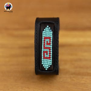 Può includere: Braccialetto in pelle nera con un design a perline rosse e turchesi. Le perline sono disposte in un motivo che compone la parola "GO".