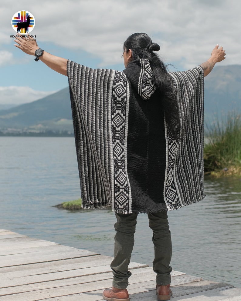 Pode incluir: Uma pessoa vestindo um poncho com capuz listrado de preto e branco com padr&otilde;es geom&eacute;tricos. O poncho &eacute; feito de l&atilde; de alpaca e tem um design tradicional. A pessoa est&aacute; em p&eacute; em um p&iacute;er de madeira com vista para um lago.