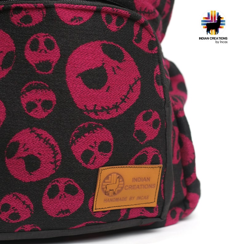 K&ouml;nnte beinhalten: Schwarzer Rucksack mit einem pinkfarbenen und schwarzen Muster von Jack Skellingtons Gesicht. Der Rucksack hat einen braunen Lederfleck mit dem Text "INDIAN CREATIONS HANDMADE BY INCAS".