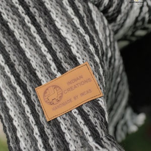 Pode incluir: Uma manta de l&atilde; de alpaca listrada em preto e branco com uma etiqueta de couro marrom que diz "INDIAN CREATIONS HANDMADE BY INCAS".