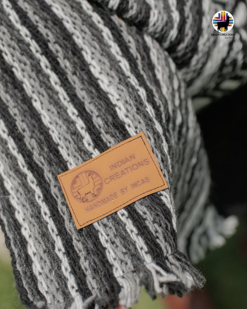 Pode incluir: Uma manta de l&atilde; de alpaca listrada em preto e branco com uma etiqueta de couro marrom que diz "INDIAN CREATIONS HANDMADE BY INCAS".