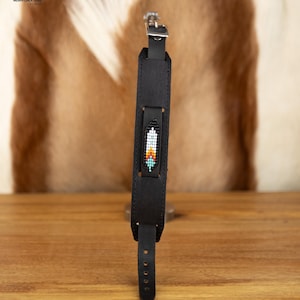 Può includere: Cinturino per fotocamera in pelle nera con un design a piuma di perline. Il cinturino ha una fibbia argentata ed è regolabile.