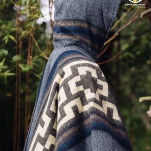 May include: A gray hooded poncho with a white and gray geometric pattern and blue stripes. The poncho is made of alpaca wool and is a traditional garment from the Andes Mountains.