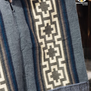 May include: Gray hooded poncho with a geometric pattern in white, brown, and blue. The poncho has a fringe border.
