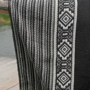 Pode incluir: Poncho de l&atilde; de alpaca listrado em preto e branco com uma borda de padr&atilde;o geom&eacute;trico. O poncho &eacute; feito no Peru.