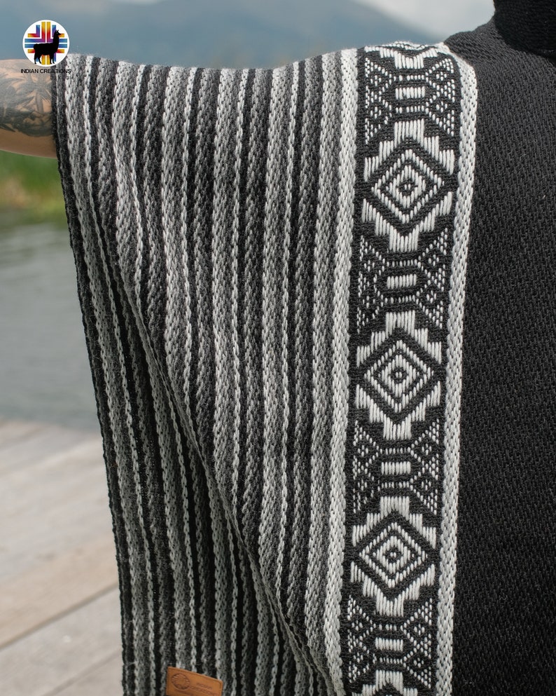 Pode incluir: Poncho de l&atilde; de alpaca listrado em preto e branco com uma borda de padr&atilde;o geom&eacute;trico. O poncho &eacute; feito no Peru.