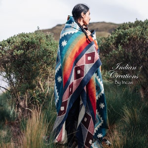Peut inclure: Une personne portant une couverture tissée colorée avec un motif géométrique. La couverture est bleue, rouge, blanche et orange. La personne se tient dans un champ d'herbe haute. Le texte "Indian Creations By Incas" est visible dans le coin inférieur droit de l'image.