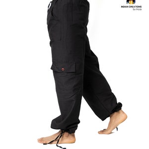 May include: Black cargo pants with a drawstring waist and a tie at the bottom of the legs. The pants have a large cargo pocket on the left leg.