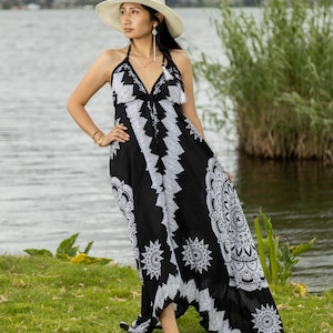 Puede incluir: Vestido halter con estampado en blanco y negro con una silueta fluida. El vestido presenta un escote en V y diseños blancos intrincados. Un sombrero crema de ala ancha completa el look. Adecuado para un ambiente informal o de resort.