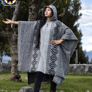Pode incluir: Um poncho cinza e preto com capuz e um padrão geométrico. O poncho é feito de lã de alpaca e tem uma bainha franjada.