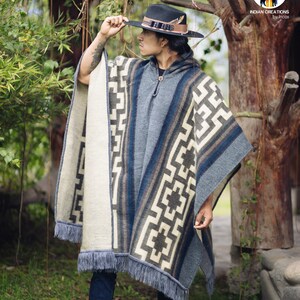 May include: A person wearing a blue and white patterned poncho with fringe. The poncho has a hood and is made of a soft, warm material. The person is wearing a black hat with a feather.