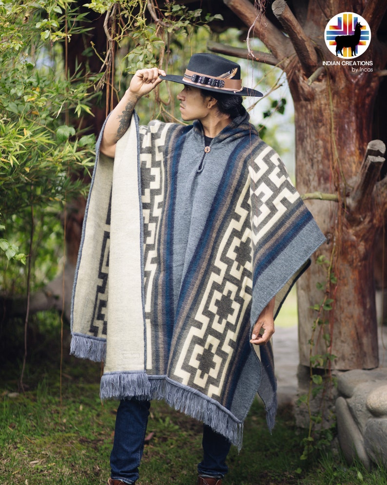 May include: A person wearing a blue and white patterned poncho with fringe. The poncho has a hood and is made of a soft, warm material. The person is wearing a black hat with a feather.