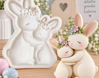 Könnte beinhalten: Eine weiße Silikonform mit zwei sich umarmenden Hasen, die jeweils einen Blumenkranz tragen, neben einer fertigen Figur im gleichen Design. Die Figur ist cremefarben mit rosa Wangen und einem Kranz aus blauen, rosa und violetten Blumen.
