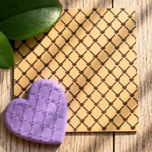 May include: A light purple heart-shaped object with a textured grid pattern featuring small raised dots at each intersection, placed next to a square card with a matching dark brown grid pattern on a light tan background.