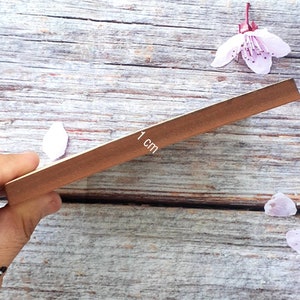 K&ouml;nnte beinhalten: Nahaufnahme eines Holzlineals mit brauner Oberfl&auml;che. Das Lineal ist 1 cm breit und hat ein wei&szlig;es Etikett mit dem aufgedruckten Text "1 cm".