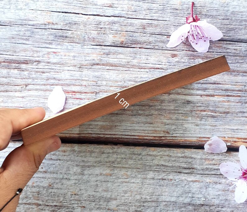 K&ouml;nnte beinhalten: Nahaufnahme eines Holzlineals mit brauner Oberfl&auml;che. Das Lineal ist 1 cm breit und hat ein wei&szlig;es Etikett mit dem aufgedruckten Text "1 cm".