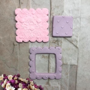 Può includere: Tre decorazioni in fondente rosa e viola. Un quadrato rosa con bordo smerlato con ombrelli, cuori e arcobaleni in rilievo. Un quadrato viola con motivo a cuore e una cornice smerlata viola completano il set.