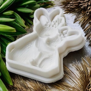 May include: A white, detailed silicone mold in the shape of a floral design. The mold has a rectangular base and features a raised, textured floral pattern. The mold is designed for crafting and creating decorative elements.