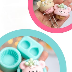 Puede incluir: Dos moldes de silicona para hacer dijes con forma de cupcake. Un molde es un molde redondo único con una superficie texturizada. El otro molde tiene dos cavidades, cada una con forma de cupcake. Un dije de cupcake rosa con cara de oso y hojas verdes se muestra en una de las cavidades del molde.