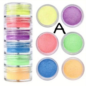 May include: A set of seven small jars of colorful glitter powder. The jars are arranged in a circle with the letter "A" in the center. The colors are yellow, purple, pink, green, blue, and orange.