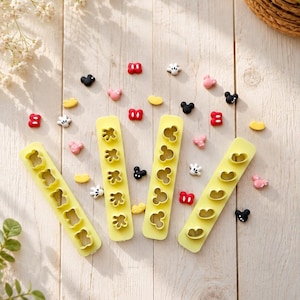 May include: Four yellow rectangular plastic moulds with various cutout shapes including bear silhouettes, hand outlines, and circular character heads, surrounded by small, colourful, three-dimensional character-themed embellishments.