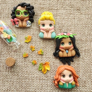 May include: Four handmade polymer clay figurines of cartoon characters with large eyes. The characters are all wearing different outfits and have different hair colors. The figurines are sitting on a brown burlap background.