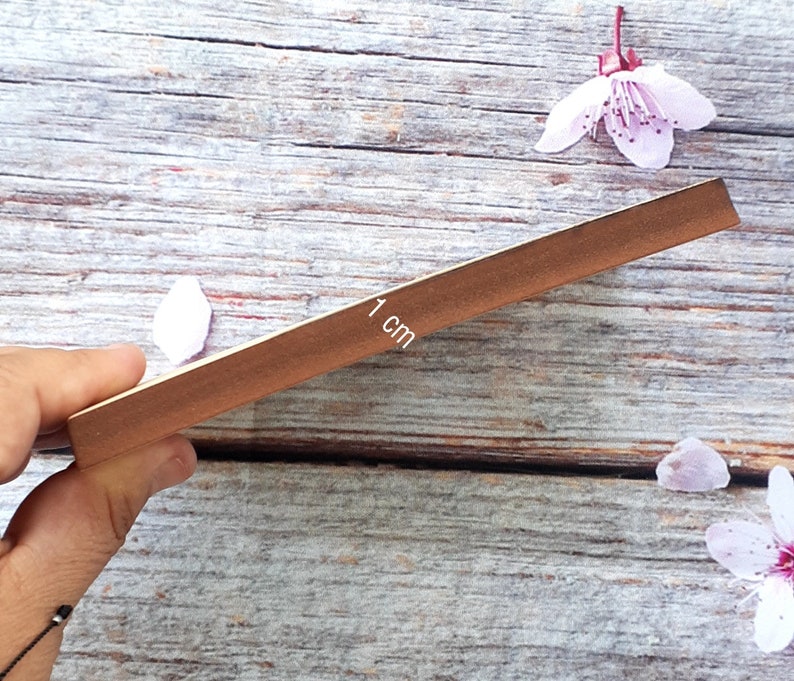 May include: A close-up of a wooden ruler with a brown finish. The ruler is marked with "1 cm" and is being held by a hand.