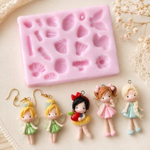 Puede incluir: Un molde de silicona rosa rectangular con varias formas peque&ntilde;as en relieve para manualidades, acompa&ntilde;ado de cinco dijes en miniatura con tem&aacute;tica de hadas, incluyendo dos pendientes con figuras de pelo amarillo y tres colgantes de personajes.