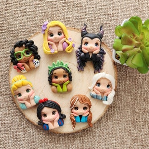 May include: A set of eight handmade polymer clay figurines of Disney princesses and villains. The figurines are all in a sitting pose with their heads tilted down. The figurines are all different colors and have different facial expressions.