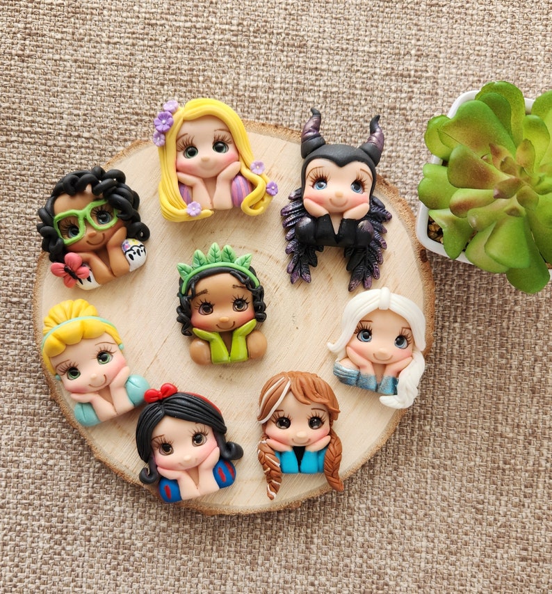 May include: A set of eight handmade polymer clay figurines of Disney princesses and villains. The figurines are all in a sitting pose with their heads tilted down. The figurines are all different colors and have different facial expressions.
