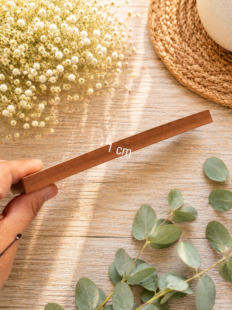 May include: A rectangular wooden block with a smooth, medium-brown finish. The side of the block is clearly marked with the text 1 cm, indicating its thickness. The object is held at an angle, showcasing its solid construction and flat edges.