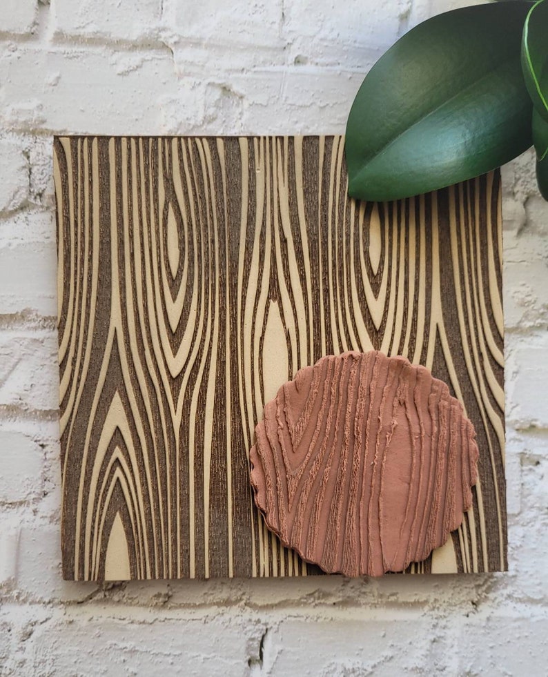 May include: A brown woodgrain patterned board with a smaller, raised, pink woodgrain patterned oval shape in the center.