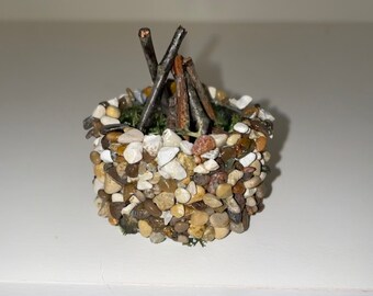 May include: A miniature campfire made of small stones and twigs, with a green moss base.