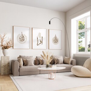 May include: A modern living room featuring three framed art prints with gold calligraphy. The prints hang above a beige sofa with patterned pillows. A white rug, a round coffee table, and a curved floor lamp complete the decor.
