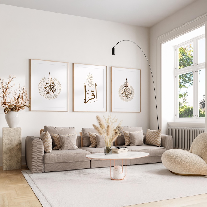 May include: A modern living room featuring three framed art prints with gold calligraphy. The prints hang above a beige sofa with patterned pillows. A white rug, a round coffee table, and a curved floor lamp complete the decor.