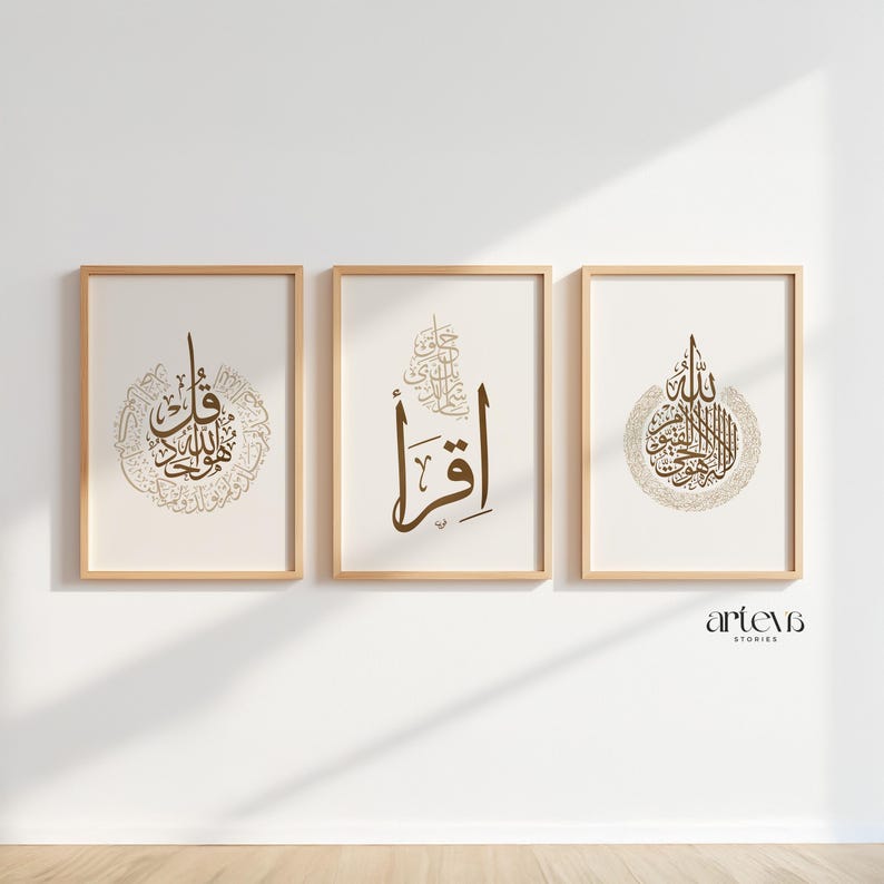 May include: Three framed art prints with Arabic calligraphy in brown tones. The prints are displayed on a white wall with a wooden floor. The frames are made of light wood. The calligraphy is in a decorative style.
