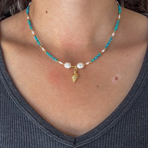 May include: A turquoise and white beaded necklace with a gold seashell charm and two white pearl accents.