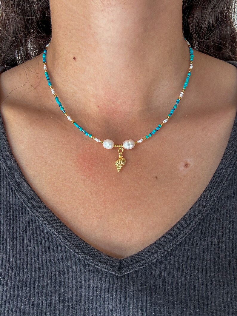 May include: A turquoise and white beaded necklace with a gold seashell charm and two white pearl accents.