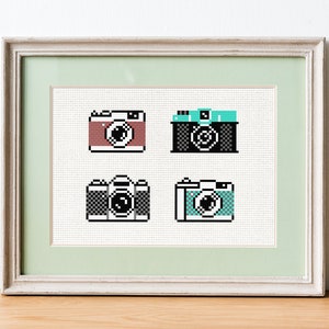 Puede incluir: Cuatro imágenes de estilo pixel art de cámaras en un marco blanco con un paspartú verde claro. Las cámaras son de color rojo, negro, blanco y negro y azul.