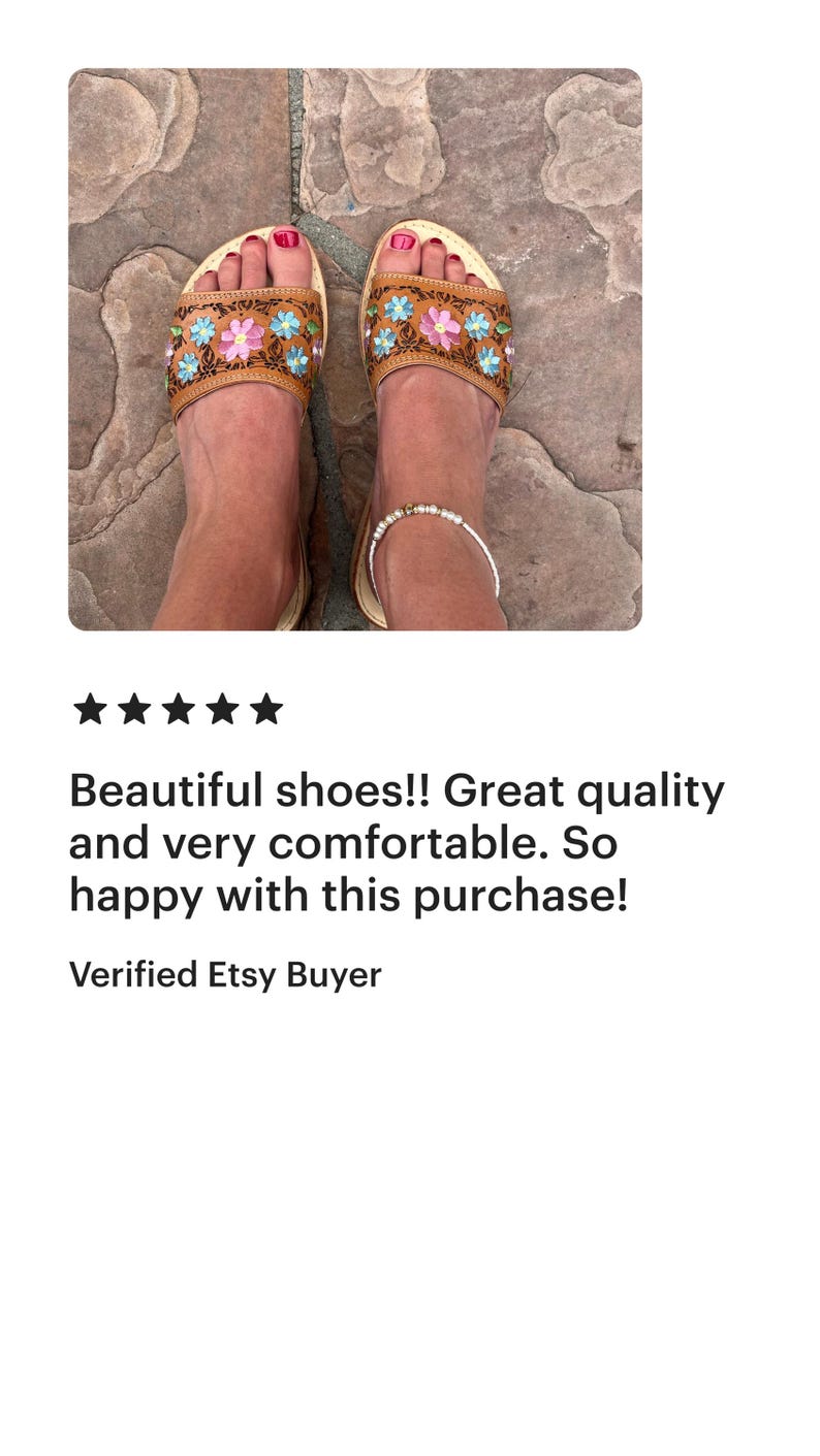 May include: A pair of brown leather sandals with floral embroidery in pink, blue, and yellow. The sandals have a light-colored sole and are worn on a stone surface. The text "Beautiful shoes!! Great quality and very comfortable. So happy with this purchase!" is also visible.