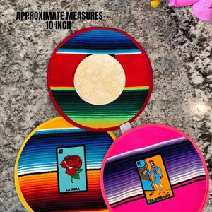 K&ouml;nnte beinhalten: Drei runde, farbenfrohe Tischsets mit traditionellem mexikanischem Serape-Design. Jedes Tischset zeigt eine andere Loteria-Karte mit einer Nummer und einem Bild. Die Karten sind "La Rosa", "La Borracha" und "El Sol". Die Tischsets haben einen Durchmesser von etwa 25 cm.
