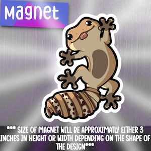 May include: A gecko magnet with a cartoon illustration. The gecko is tan and brown with a striped tail and is sticking out its tongue. The word "Magnet" is in a blue and purple banner. The magnet is approximately 7.6 cm in height or width.